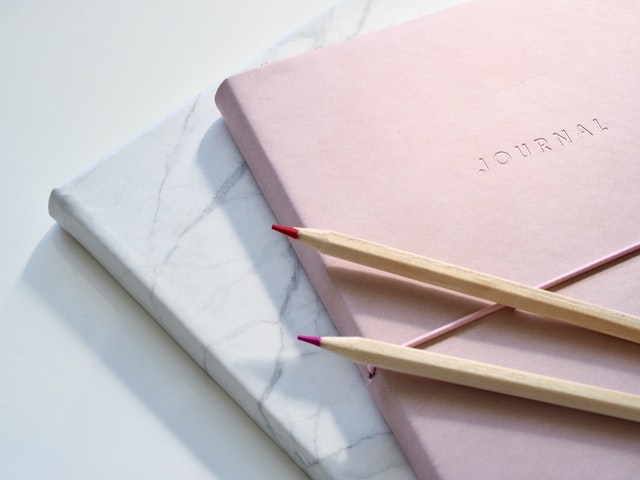 Two pencils kept on a Pink colored Journal. 